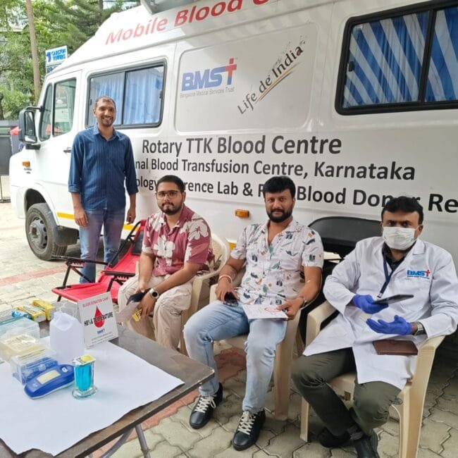 Volunteers and staff at The Yard's blood donation drive with the Rotary TTK Blood Centre mobile blood collection van, alongside donor screening equipment including a hemoglobin testing kit
