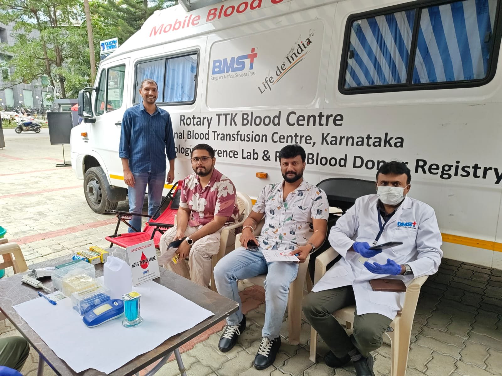 Volunteers and staff at The Yard's blood donation drive with the Rotary TTK Blood Centre mobile blood collection van, alongside donor screening equipment including a hemoglobin testing kit