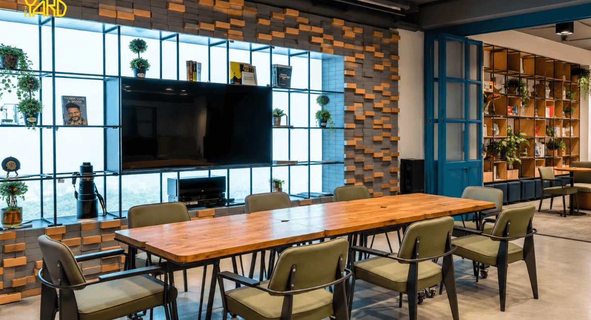 Meeting room with wooden table, green chairs and TV wall at The Yard coworking space