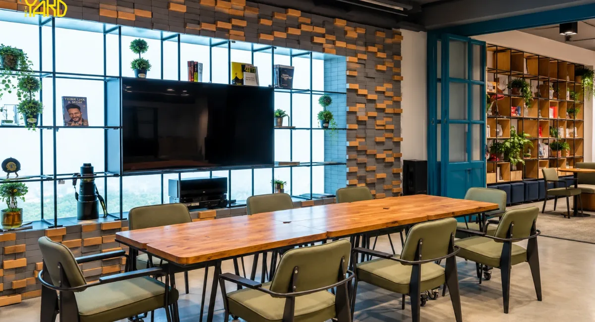 Meeting room with wooden table, green chairs and TV wall at The Yard coworking space