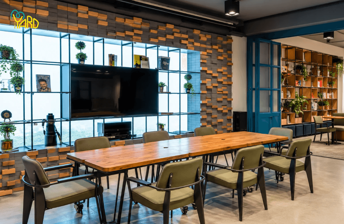 Meeting room with wooden table, green chairs and TV wall at The Yard coworking space