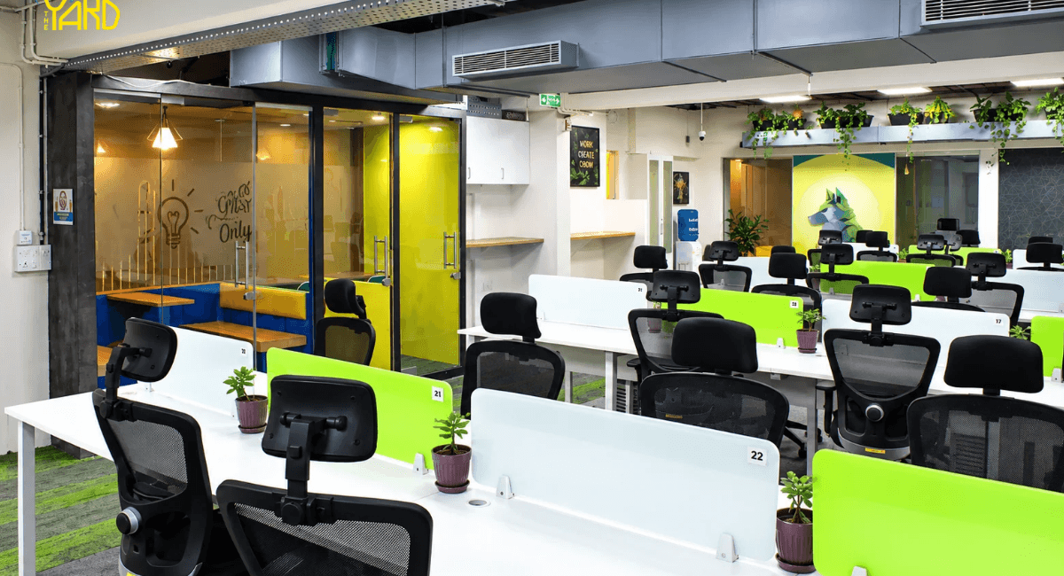 Numbered open desk workstations with green dividers and plants at The Yard coworking space