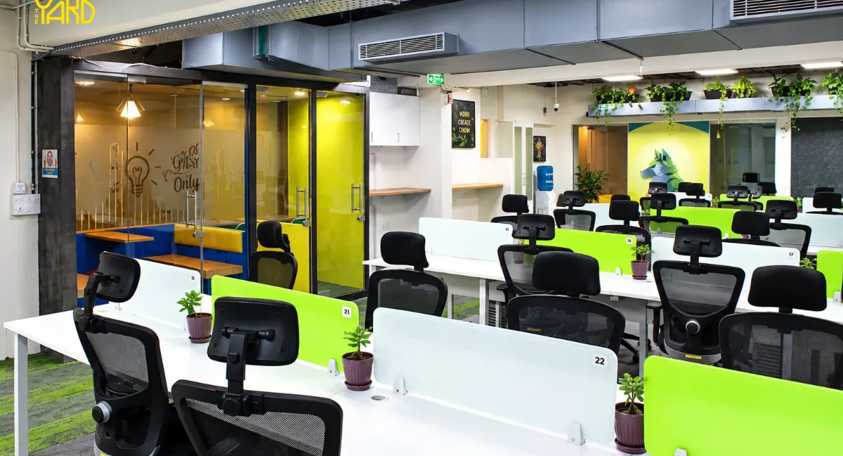 Numbered open desk workstations with green dividers and plants at The Yard coworking space