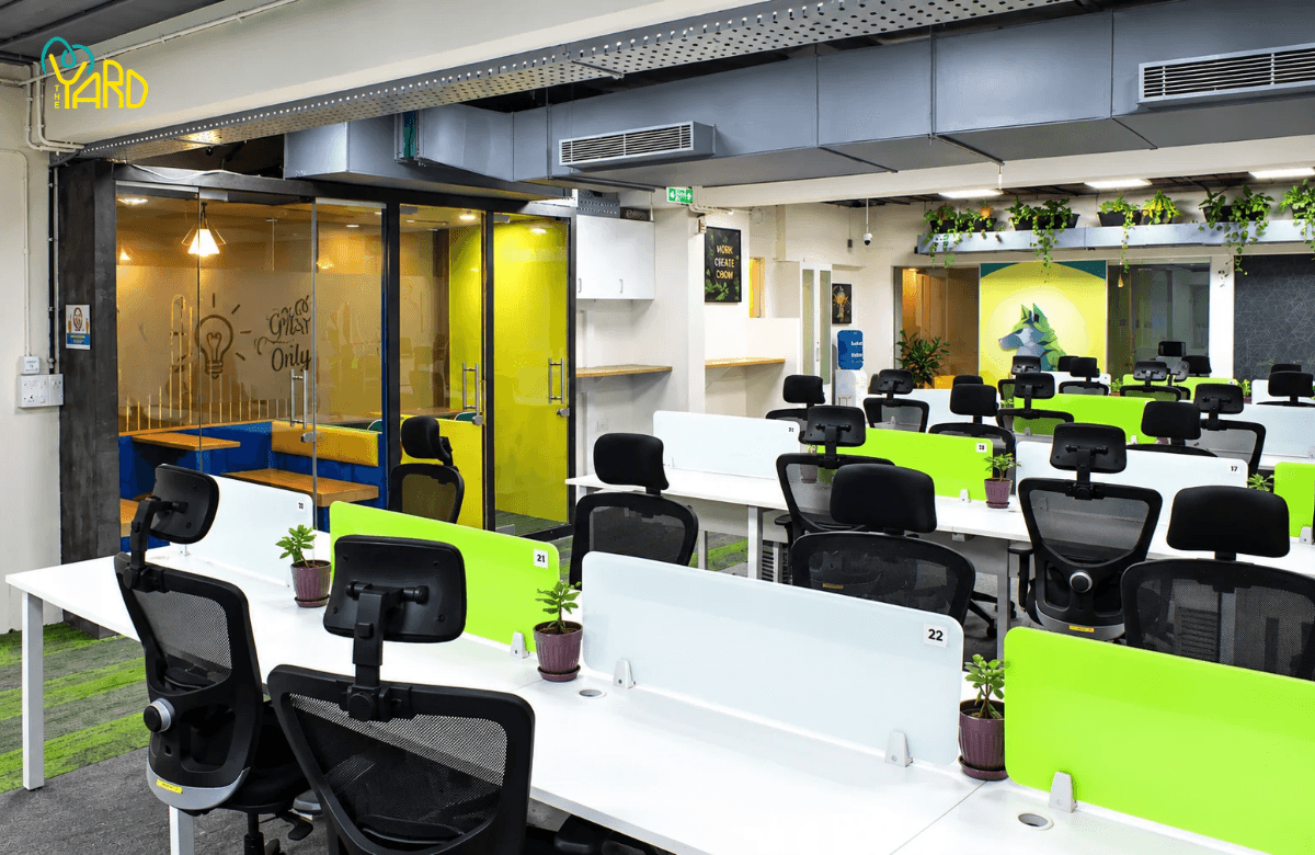 Numbered open desk workstations with green dividers and plants at The Yard coworking space