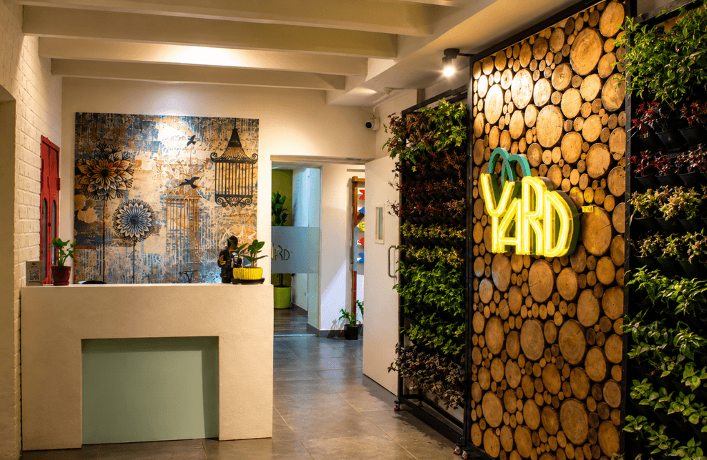 Reception area with neon Yard sign and plant wall at The Yard coworking space