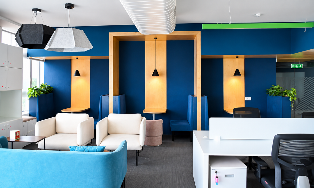 Modern coworking workspace with blue walls, private seating booths, comfortable sofas and office desks