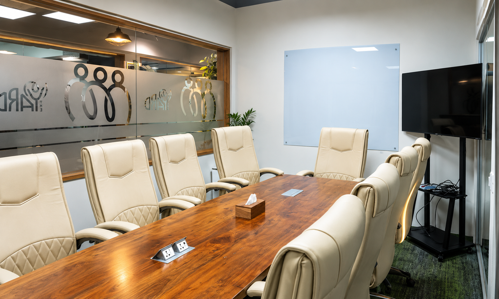 Large meeting room with wooden table, leather chairs and TV screen at The Yard coworking space