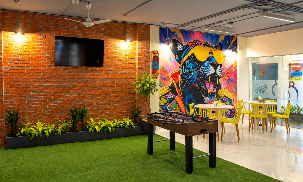 Coworking lounge with colourful wall art, yellow chairs, indoor plants and a foosball table